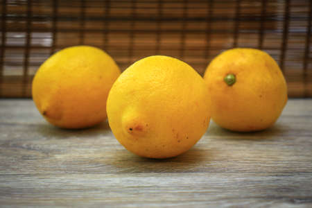 Three lemons on a light wooden table top.Three lemons on a light wooden tabletop replacing the...