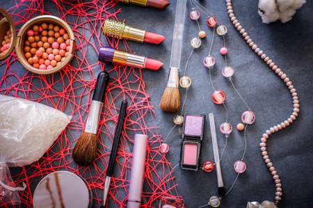 Women's cosmetics on a dark graphite background: pink lipstick of 3 shades, pink and peach eyeshadow, polka-dot powder, salt for baths, nail polish gently pink, mascara, a string of pink pearls.の写真素材