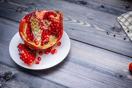 Pomegranate sliced on a white plate against a graphite wooden tabletopの写真素材