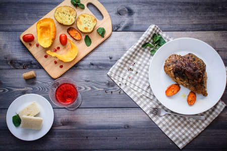 A piece of meat, sprinkled with spices, baked with baked carrot slices on a white plate, fork, linen checkered napkin, next to the baked slices of pumpkin, potatoes, spices and cherry tomatoes.の写真素材
