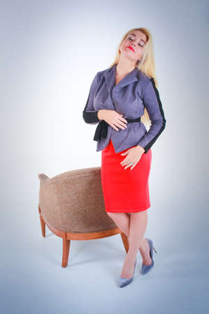 White to light blue gradient background. The girl in a red skirt in a gray jacket put next to the chair threw back her head.の写真素材