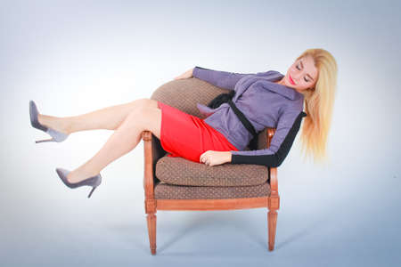 White to light blue gradient background. A girl in a red skirt in a gray jacket lies on a chair side view.の写真素材