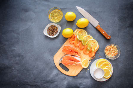 Raw fish with seasonings. On a wooden board laid out salmon raw shrimp greens lemon slices salt...