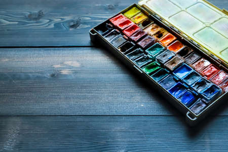 On a dark gray wooden tabletop, juicy watercolor paints, which the artist already used, are open.
Wooden paint table many different colors watercolor.の写真素材