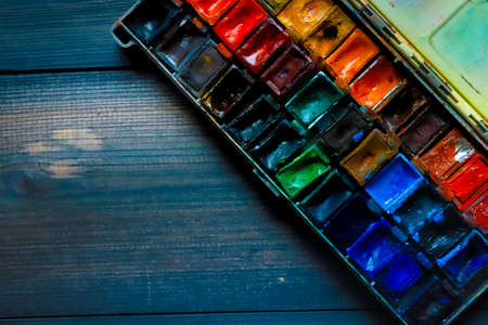 On a dark gray wooden tabletop, juicy watercolor paints, which the artist already used, are open.
Wooden paint table many different colors watercolor.の写真素材