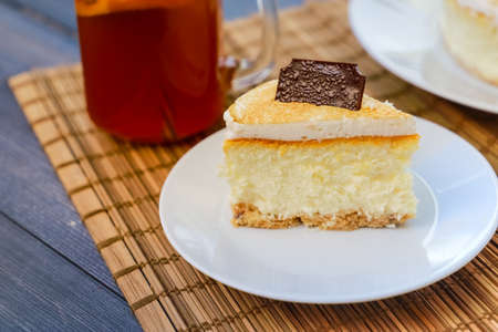 Classic cheesecake cake on a dish, a piece of cake on a saucer, a spoon, tea in a mug, everything on...