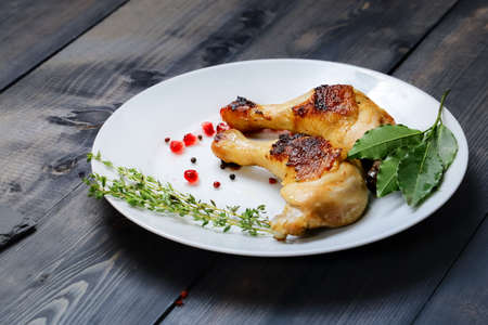 On a white dish on a dark wooden tabletop are two fried chicken legs with sprigs of thyme and bay leaf.の写真素材