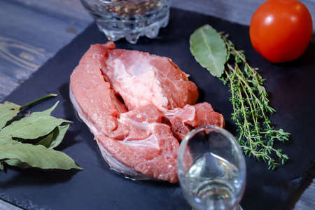 On a graphite-colored stone stand there is a piece of raw bright beef decorated with peas of...