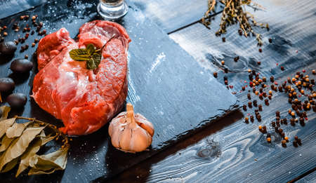 On a dark countertop, a large piece of raw beef, garnished with bay leaves, pepper, in a sauceboat butter and garlic thymeの写真素材