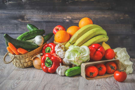 Vegetables and fruits on a graphite wooden background: in a box are tomatoes, cucumber, garlic,...