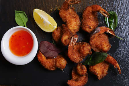 Shrimps Tempura king prawns, sliced lemon, green basil leaves are served on a black stone stand....