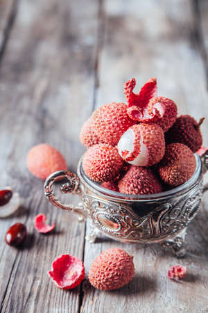 Fresh organic lychee fruit in a bowl on a rustic wooden background. Copy space.