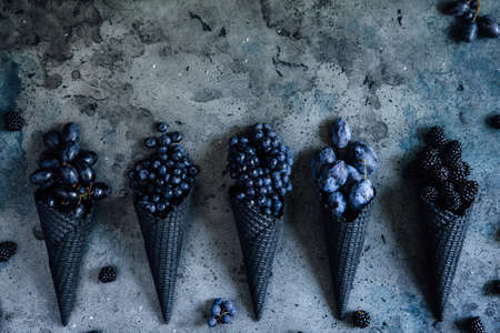 Fresh  blueberry, grapes, plum, blackberry in a waffle cone on a dark old background, toned in retro style, top view.の写真素材