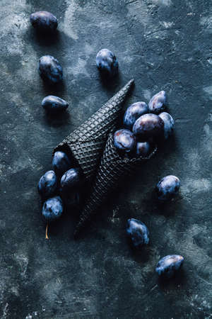 Fresh plums in a black waffle cone on a dark old background, toned in retro style, top view.の写真素材