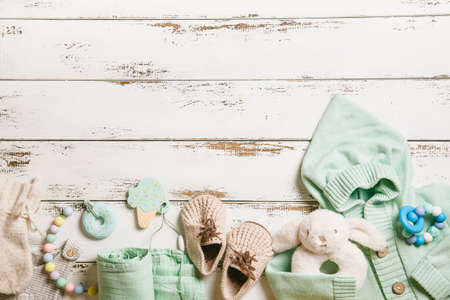 Newborn baby clothing, bootees, teethers and toy on white wooden background with copy space. Baby fashion concept. Top view, flat lay.の写真素材