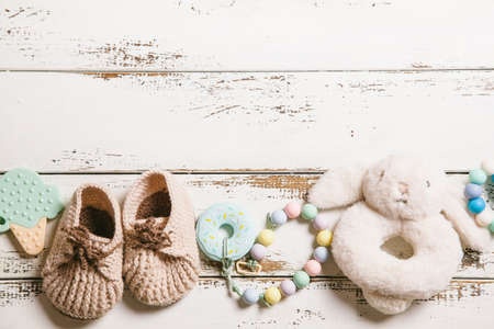 Newborn baby bootees, teethers and toy on white wooden background with copy space. Baby fashion concept. Top view, flat lay.の写真素材