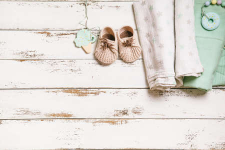 Newborn baby swaddling clothes, bootees and teethers on white wooden background with copy space. Baby fashion concept. Top view, flat lay.の写真素材