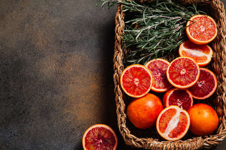 Sliced Sicilian blood oranges with sprigs of rosemary in a wicker basket on a rustic background. Top view. Flat lay, copy space.の写真素材