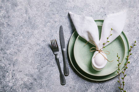 Happy easter concept. Easter bunny. Easter egg in a plate and branches with buds on a gray background. Flat lay, top view, copy space.の写真素材
