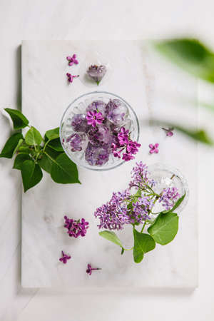 Beautiful lilac flowers frozen in ice cubes on a white marble background. Flat lay, top view, copy space.の写真素材