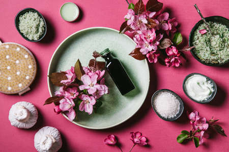 Set of natural skin care products and pink flowers in a green plate and black bowls on a pink background. Spa treatment concept. Flat lay, top view.の写真素材