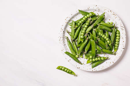 Pea pods in a white plate on a marble background. Healthy food and clean eating concept. Flat lay, top view, copy space.の写真素材