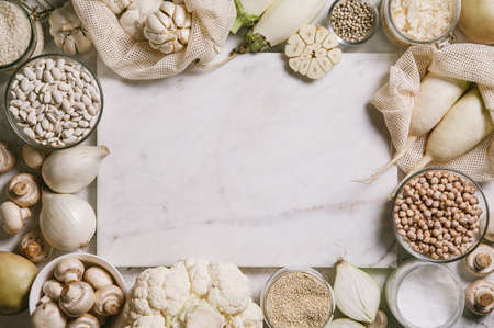 White vegetables and mushrooms, rice, quinoa, legumes, white peppercorns, coconut oil around a white marble cutting board on a white background. Healthy eating and the concept of clean eating. Flat lay, top view, copy space.の写真素材