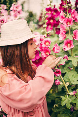 A girl in a beautiful pink dress and hat walks in a blooming garden. Image with selective focus.の写真素材