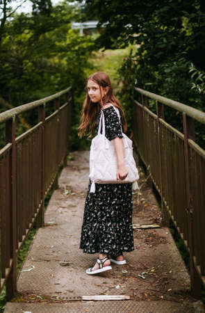 A girl in a beautiful black dress is walking on a bridge in the park. Image with selective focus.