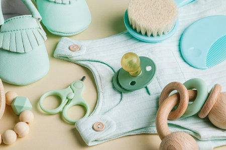 Baby care accessories, clothing and bootees. Newborn baby pacifier, teethers, nail scissors, hair brush on a beige background. Wish list or shopping overview for pregnancy. Flat lay, top view.の写真素材