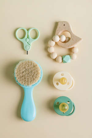 Baby care accessories. Newborn baby pacifier, teether, nail scissors, hair brush on a beige...