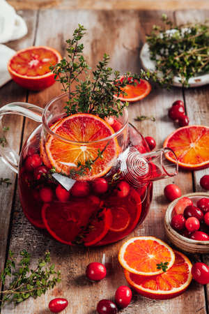 Citrus and berry tea with cranberries, blood oranges and thyme in a glass teapot on wooden table. Close up.の写真素材