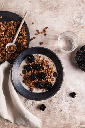 Chocolate granola with almond milk and blackberry in a black ceramic bowl on a beige background. Healthy breakfast or snack.の写真素材