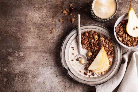 Chocolate granola with almond milk, pear and honey in a ceramic plate on a brown background. Healthy breakfast or snack.の写真素材