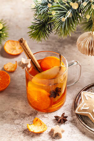 White mulled wine with tangerines, pears and cinnamon in a glass cup on a light background....
