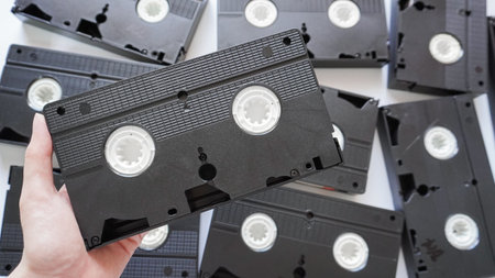 Hands holding a VHS tape back side with scattered tapes in the background.