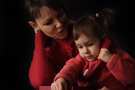 Pretty Caucasian happy mother and daughter talk on the phone on a dark background