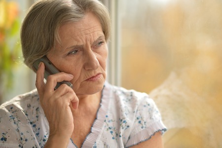Sick elderly woman calling on phone at home