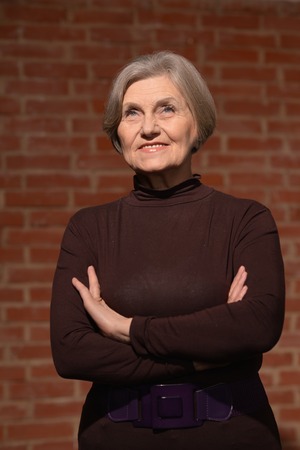 Happy smiling elder woman in elegant dress on brick backgroundの写真素材