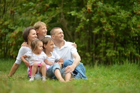 Happy family sitting on grass in summer parkの写真素材