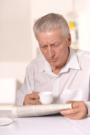 Senior man with newspaper aat home sitting at tableの写真素材