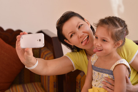 Happy mother with her daughter in summer park with phoneの写真素材