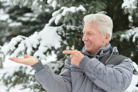 Senior man standing outdoor in winter pointing by his handの写真素材