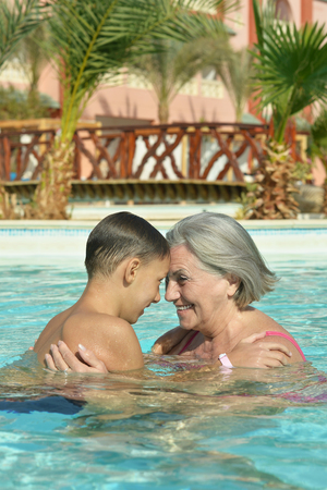 Happy smiling grandma and grandson in blue pool waterの写真素材