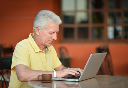 Senior man sitting with laptop in hotelの写真素材