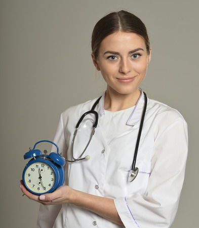Female doctor with clock, standing on grey backgroundの写真素材