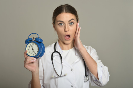 Female doctor with clock, standing on grey backgroundの写真素材
