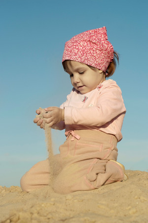 Happy little girl playing in sand on a beachの写真素材