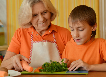 Happy elderly woman and the boy in the orange in the kitchenの写真素材