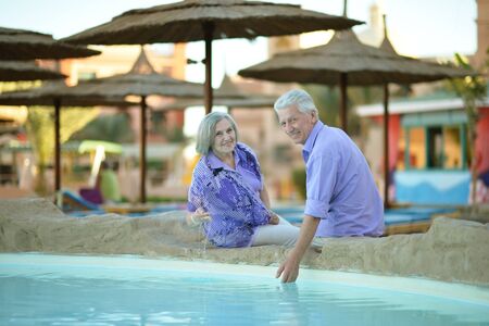 Amusing smiling old couple on vacation near swimming poolの写真素材